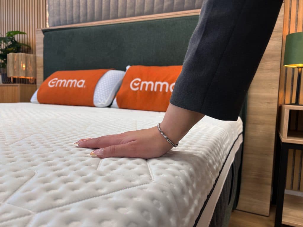 Une main teste la fermeté d'un matelas Emma en magasin
